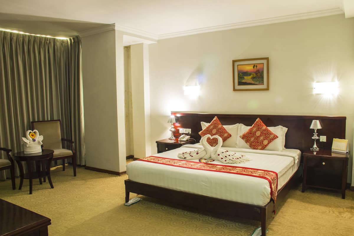 A hotel room with a large bed, a chair, a small table, and a nightstand.