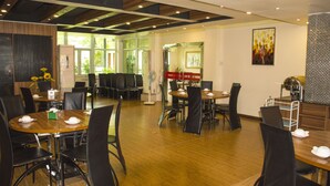 A modern dining area with wooden tables and black chairs, large windows, and a ceiling with wooden beams. - Green Leaf Hotel (Yangon)