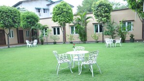 A courtyard with a white metal table and chairs, surrounded by lush green grass and trees. - Green Leaf Hotel (Yangon)
