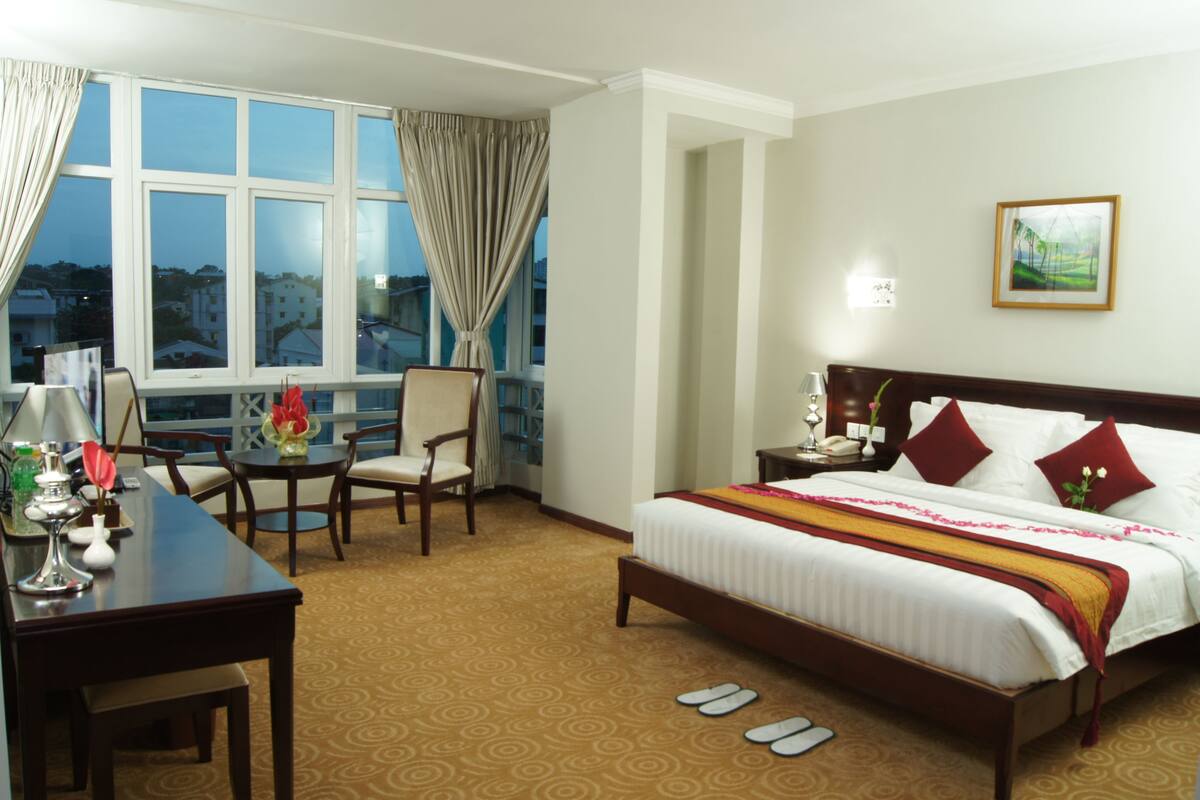A hotel room with a large bed, a desk, a chair, and a window with curtains.