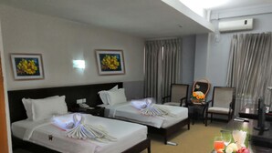 A hotel room with two beds, a desk with a fruit plate, a chair, and a desk lamp. - Green Leaf Hotel (Yangon)