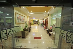 A hotel lobby with a reception desk, seating area, and a 'Welcome' mat.