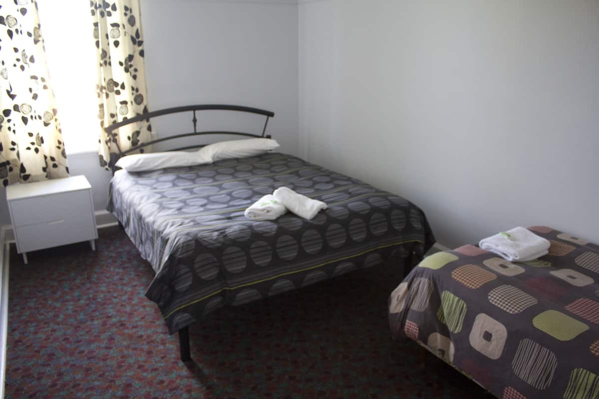 A bedroom with a single bed, a nightstand, and a window with patterned curtains.
