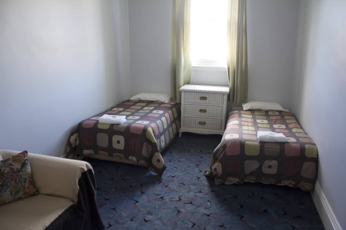 A small hotel room with two single beds, a nightstand, a chair, and a window with curtains.