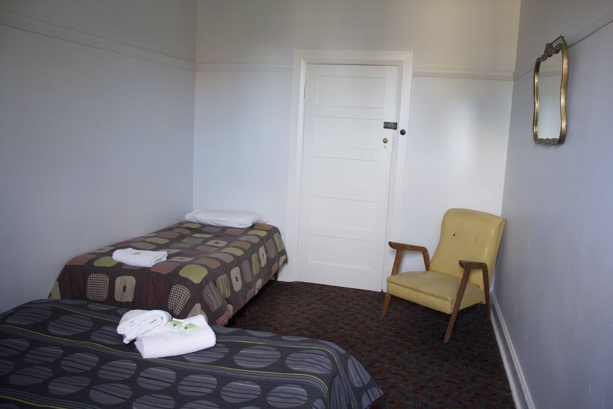 A hotel room with two beds, a chair, a door, and a mirror.
