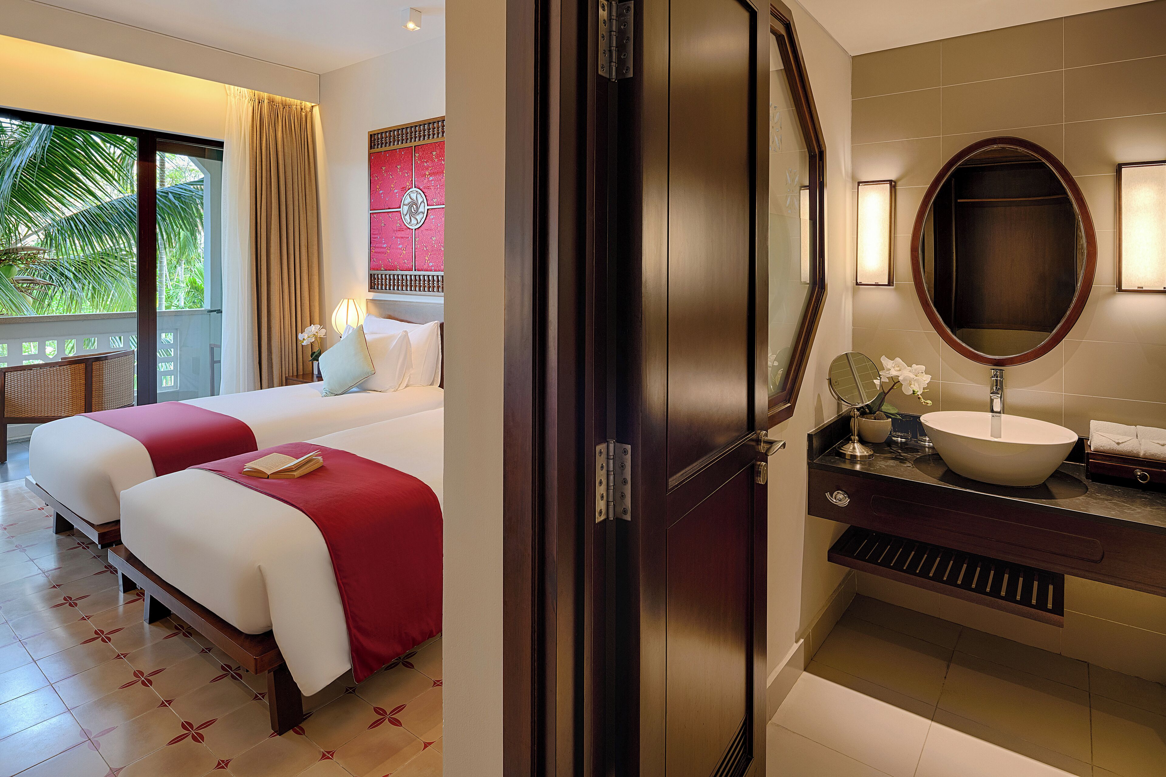 A hotel room with two beds, a large mirror, a sink, and a view of palm trees.