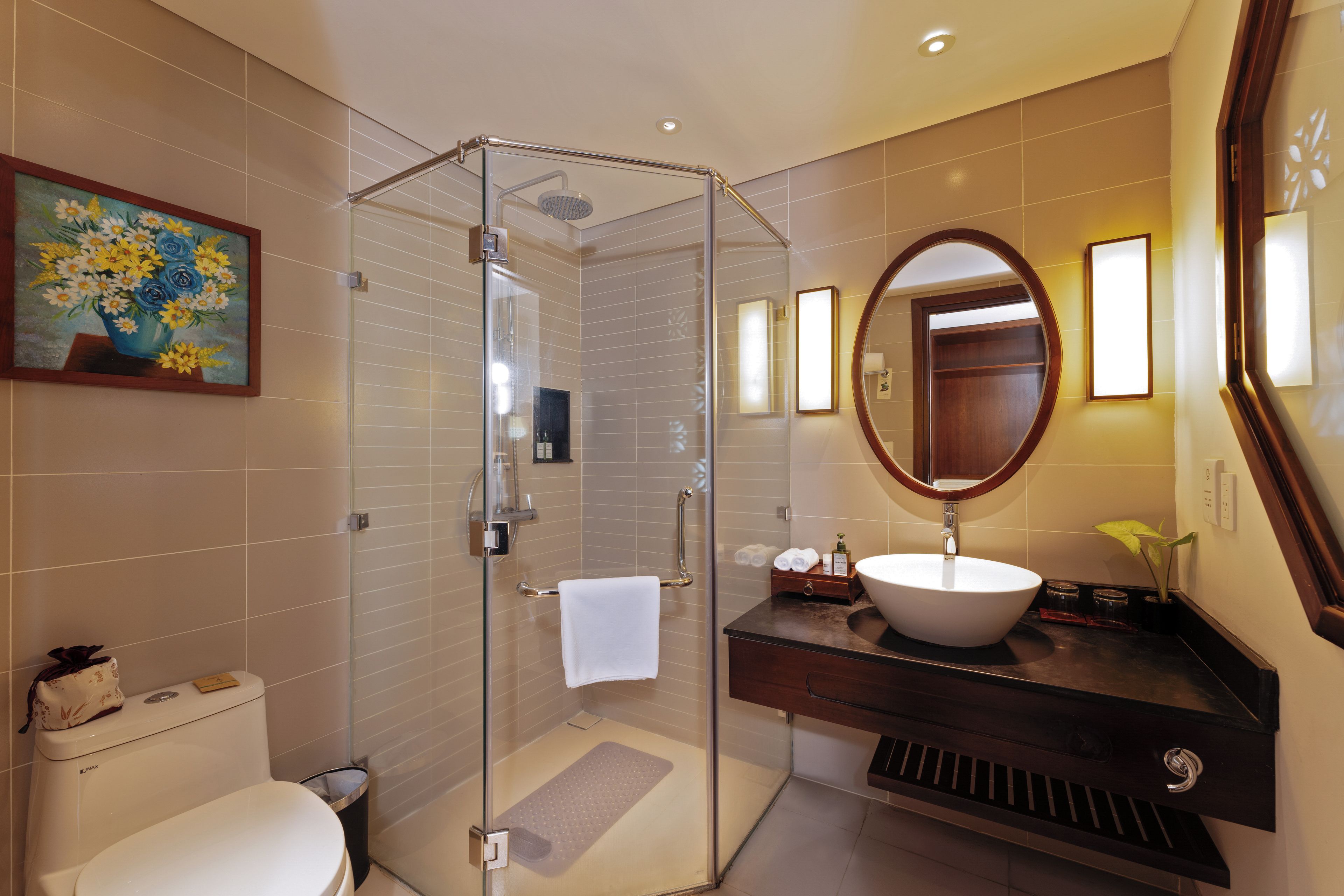 Une salle de bain moderne avec une douche à parois de verre, un grand miroir ovale et un lavabo blanc.