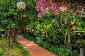 A pathway lined with trees and plants, leading to a structure with a tiled roof. - RiverTown Hoi An Resort & Spa (Da Nang)