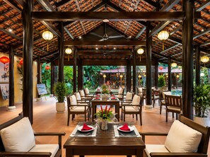 An indoor dining area with wooden tables and chairs, a ceiling fan, and hanging lanterns. - RiverTown Hoi An Resort & Spa (Hoi An)