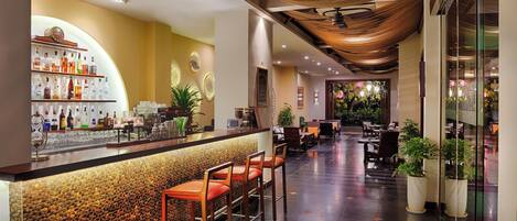 A hotel lobby with a bar area, seating, and potted plants.