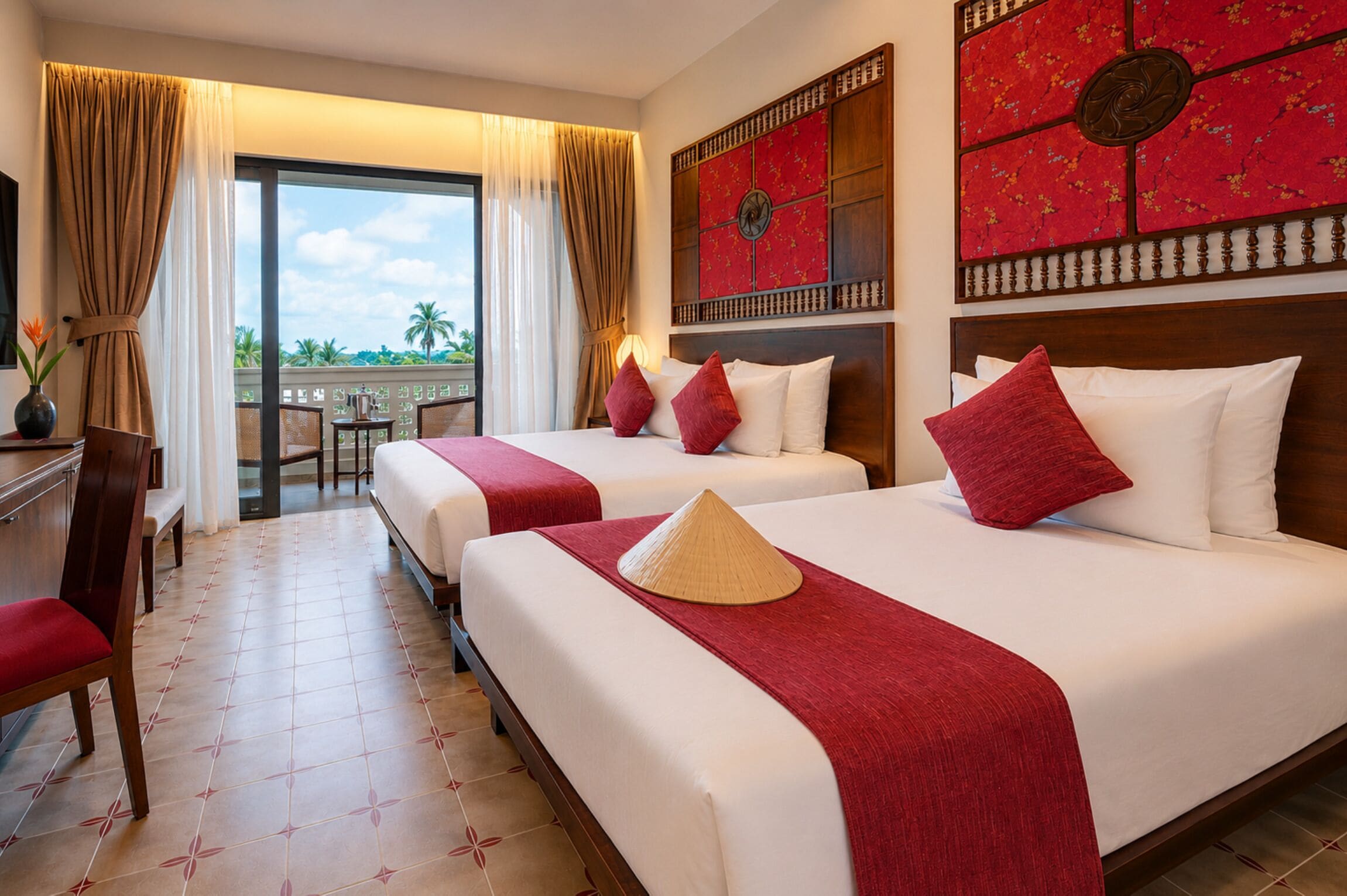 A hotel room with two beds, a desk, a chair, and a view of palm trees.