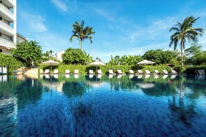 A swimming pool with lounge chairs and umbrellas, surrounded by palm trees and a building with balconies. - RiverTown Hoi An Resort & Spa (Hoi An)