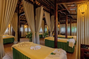 A hotel room with multiple beds, each with a green bedspread and white linens, and a large window with curtains.