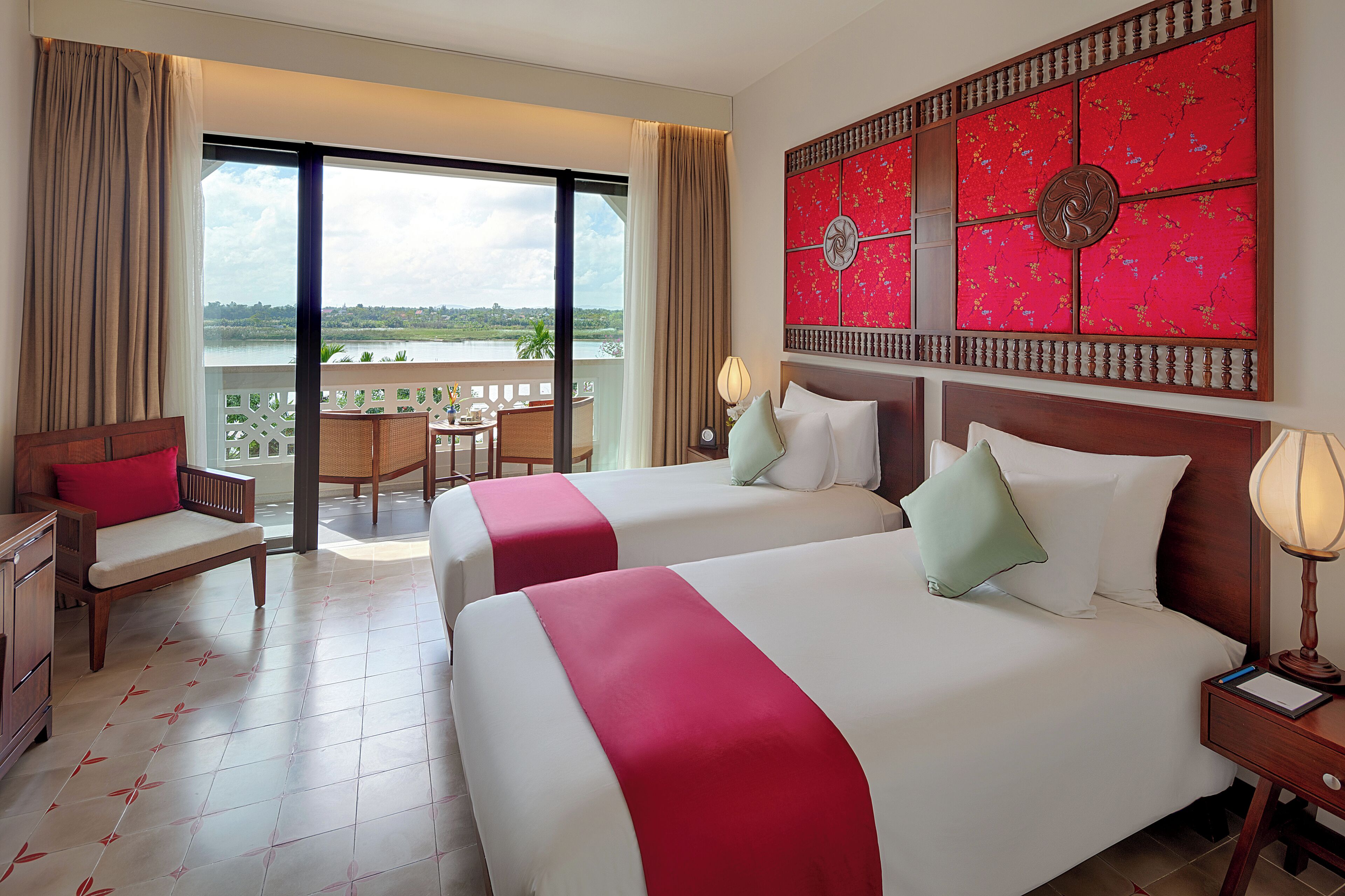 A hotel room with two beds, a balcony with a view, a wooden nightstand, and a chair.