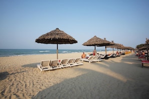 A beach with rows of sun loungers and thatched umbrellas. - RiverTown Hoi An Resort & Spa (Da Nang)