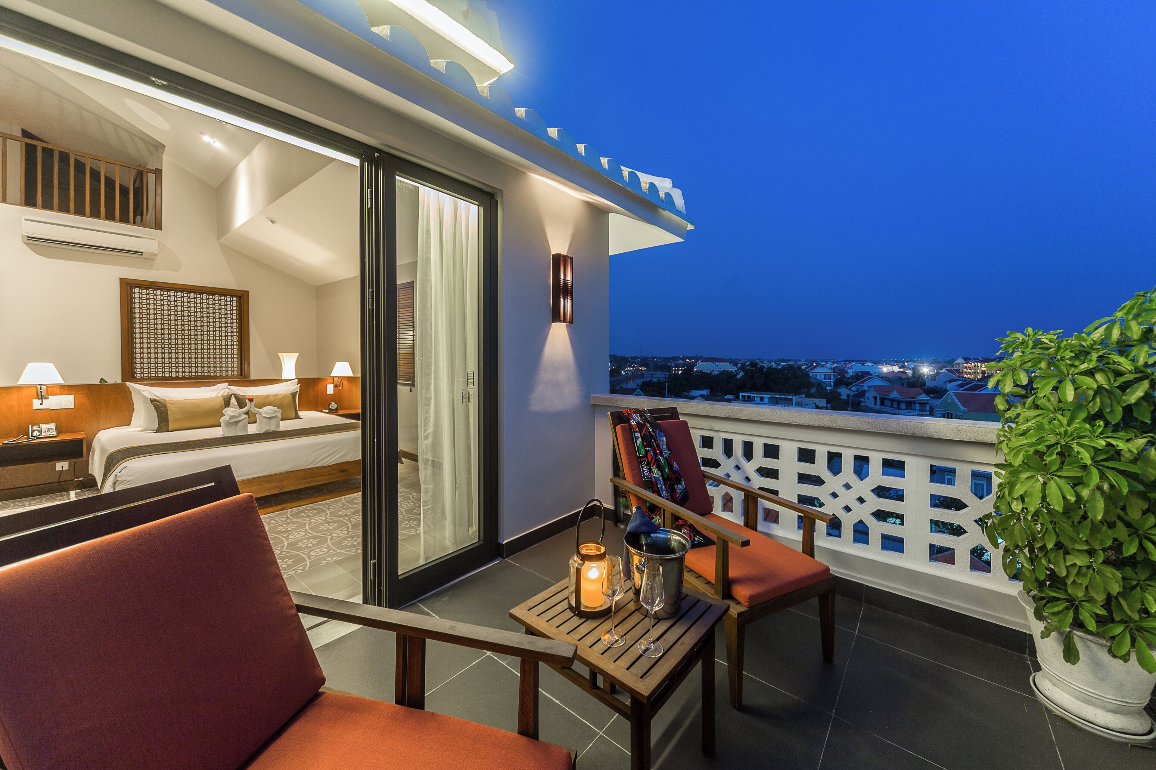 A balcony with a bed, a table with a candle, and a potted plant.