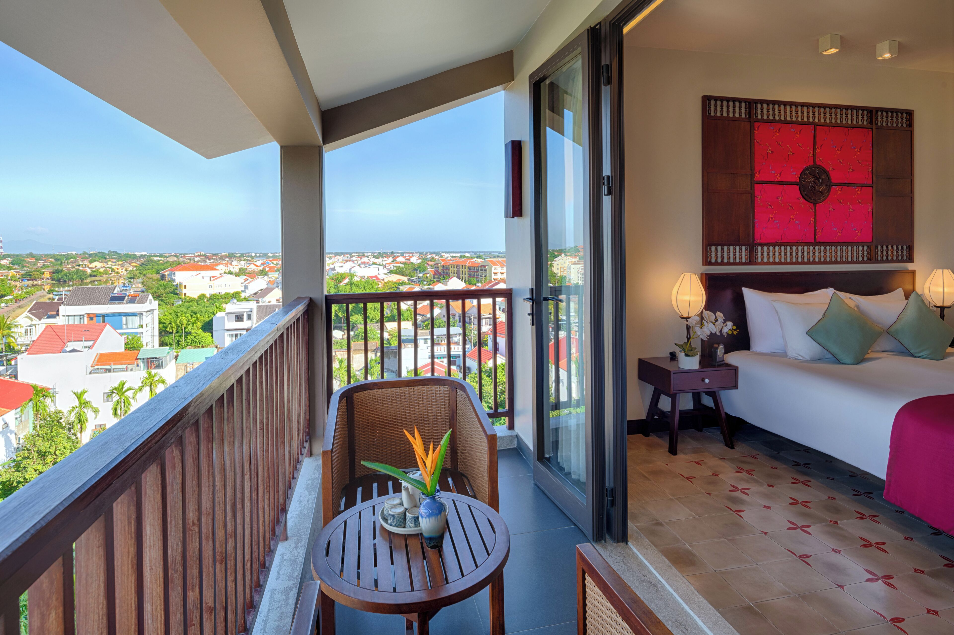 Een balkon met uitzicht op een stadsbeeld, een bed met hoofdeinde en een kleine tafel met een vaas.
