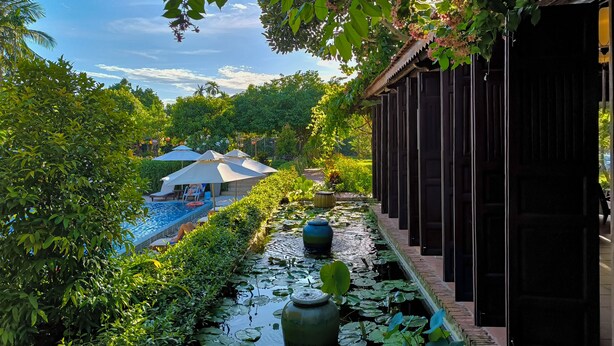Un área de piscina tranquila con nenúfares, un espacio de descanso cubierto y una estructura de madera.