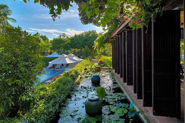 A serene pool area with water lilies, a covered seating area, and a wooden structure. - RiverTown Hoi An Resort & Spa (Da Nang)