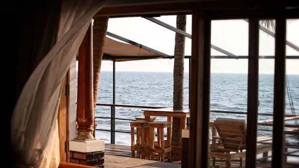 A wooden deck with a table and chairs, overlooking the sea. - 36 Palms Boutique Retreat (Kochi)