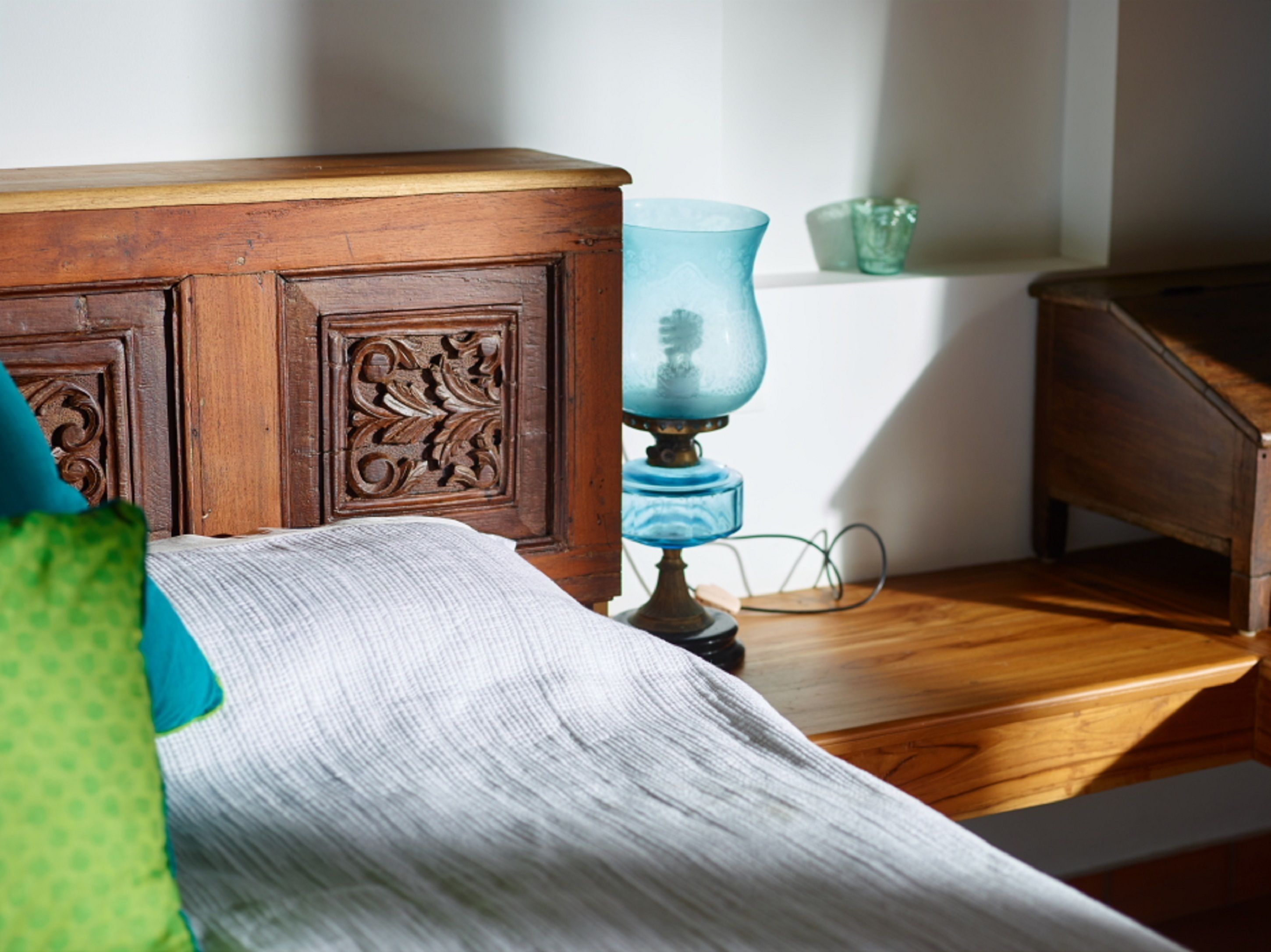 Un aparador de madera con detalles tallados, una lámpara azul y una almohada verde sobre una cama.