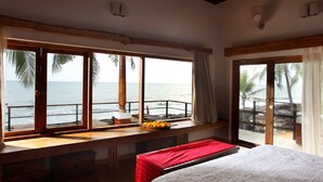 A bedroom with a large window overlooking the ocean, a bed, a small table with fruit, and a wooden bench. - 36 Palms Boutique Retreat (Kochi)