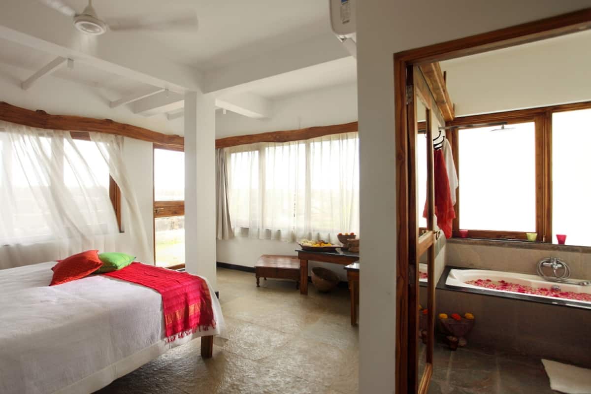 A bedroom with a bed, a desk, and a bathroom with a bathtub.