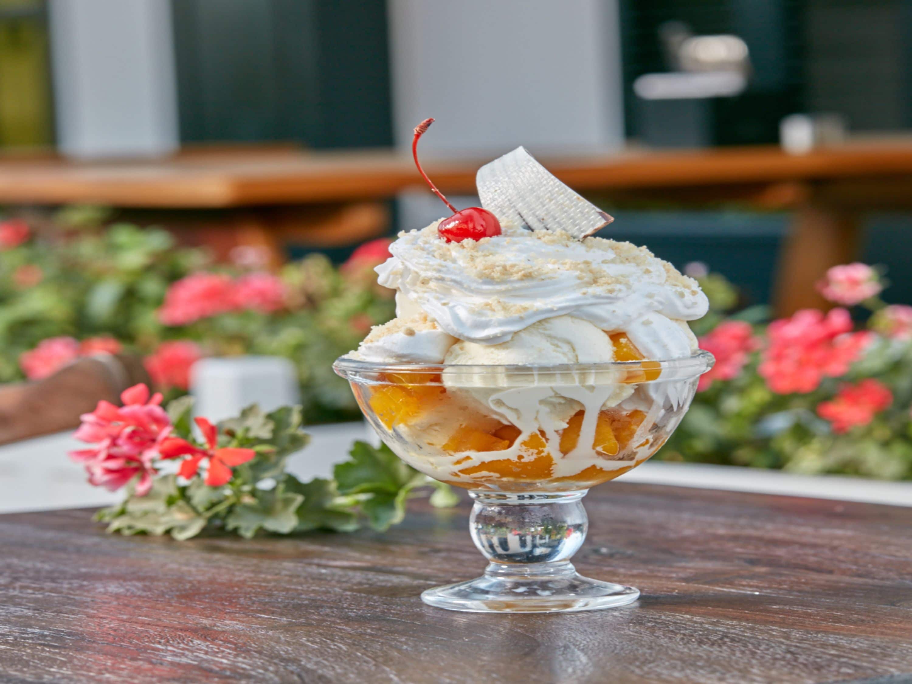 Ein Dessert in einer Glaskugel auf einem Holztisch, im Hintergrund Blumen.