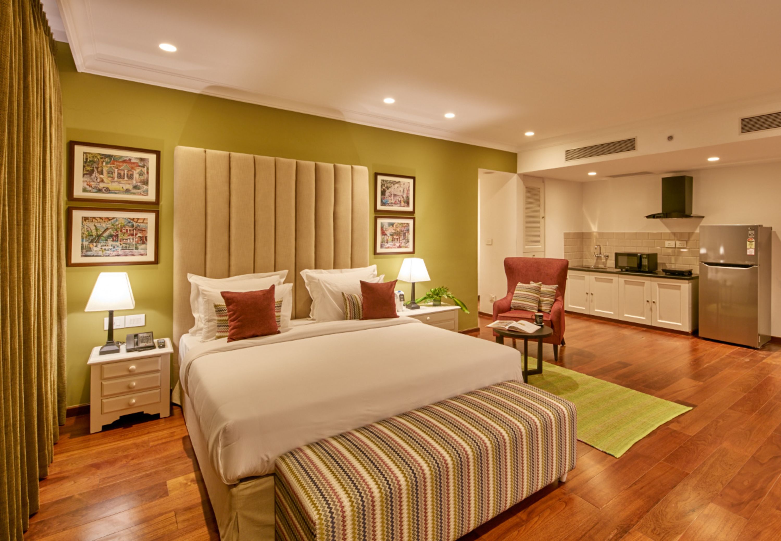 Habitación de hotel con una cama grande, un escritorio, una silla, kitchenette y obras de arte en las paredes.