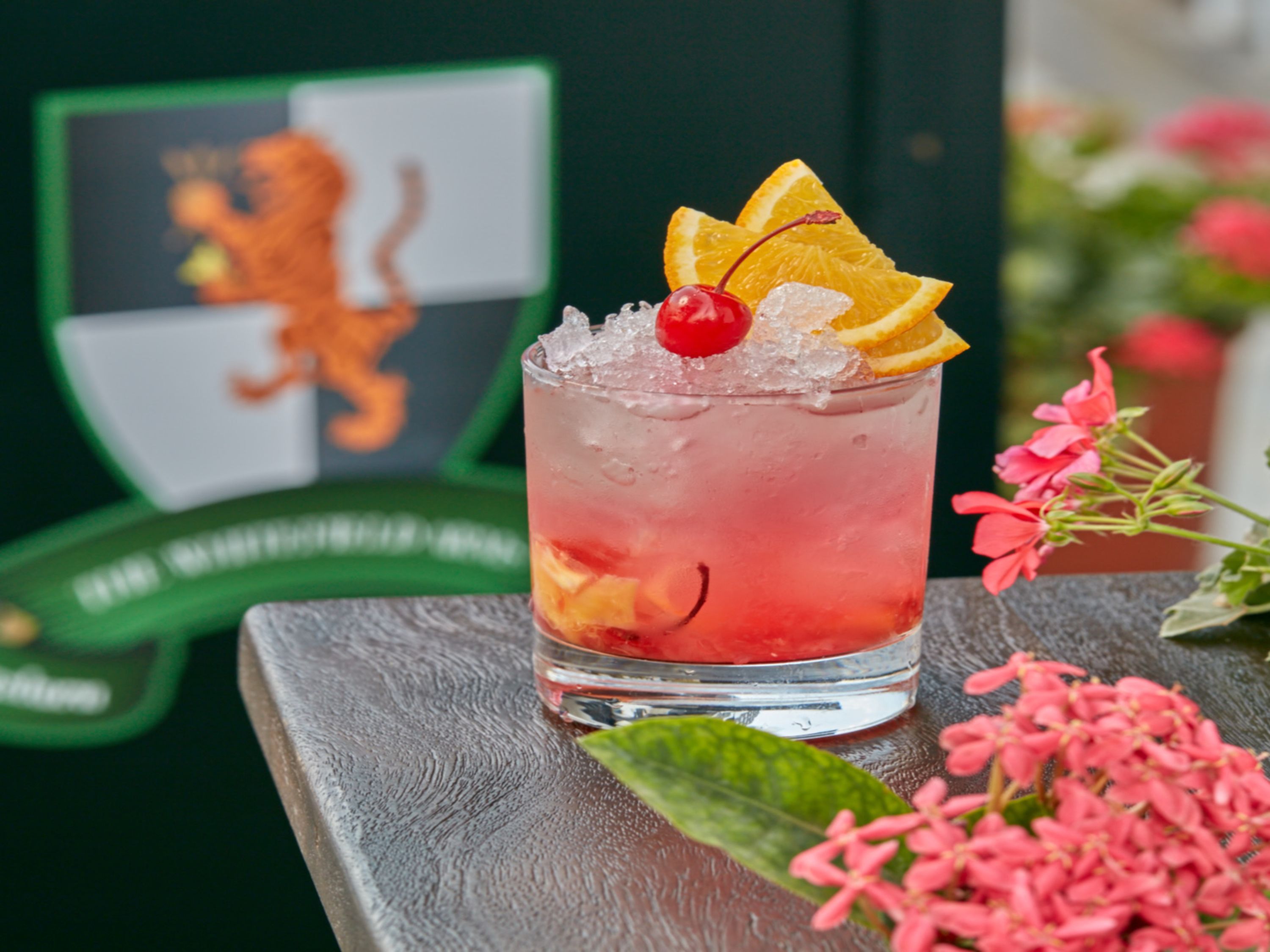 Een cocktailglas met ijs, een kers en oranjeschijfjes op een houten ondergrond.