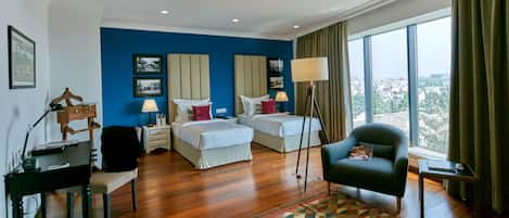 Habitación de hotel con dos camas, un escritorio, una silla y un ventanal con vistas a la ciudad.