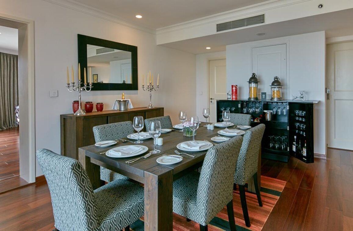 Un coin repas avec une table en bois dressée pour six personnes, entourée de chaises à motifs. Un miroir et des chandeliers sont accrochés au mur.