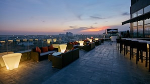 Un bar en la azotea con mesas al aire libre y vistas a la ciudad al atardecer.