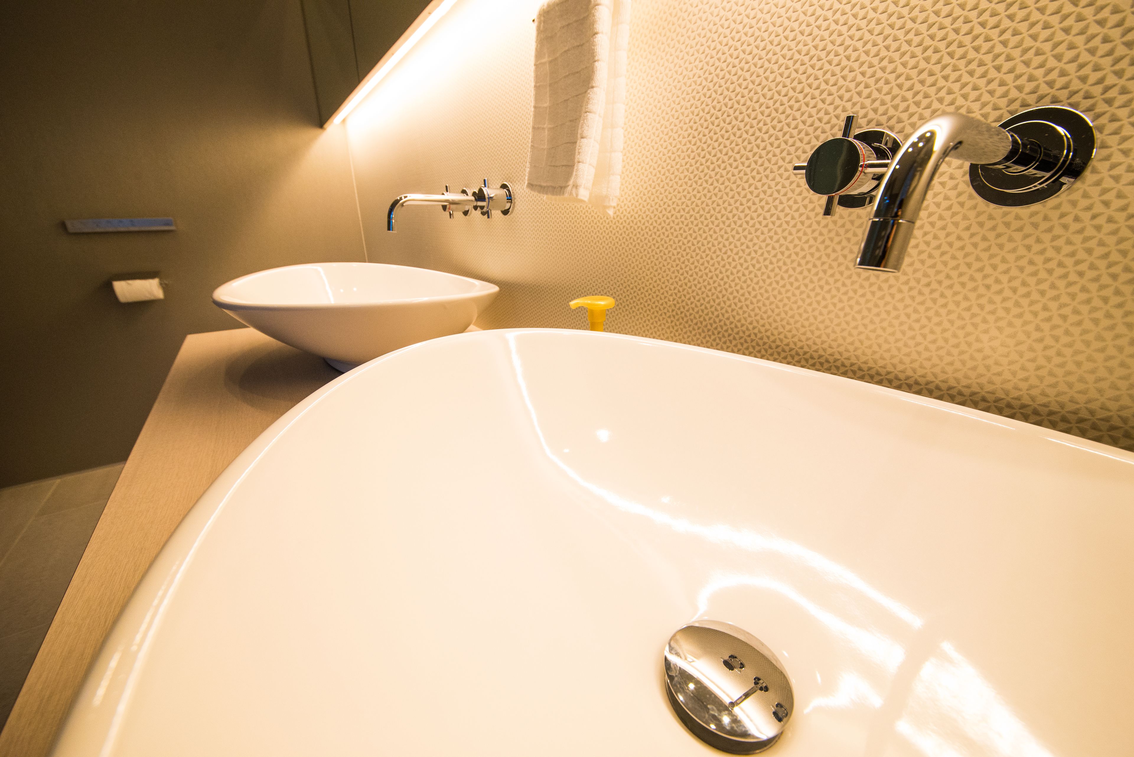 A bathroom with a large white bathtub, a white sink, and a yellow soap dispenser.