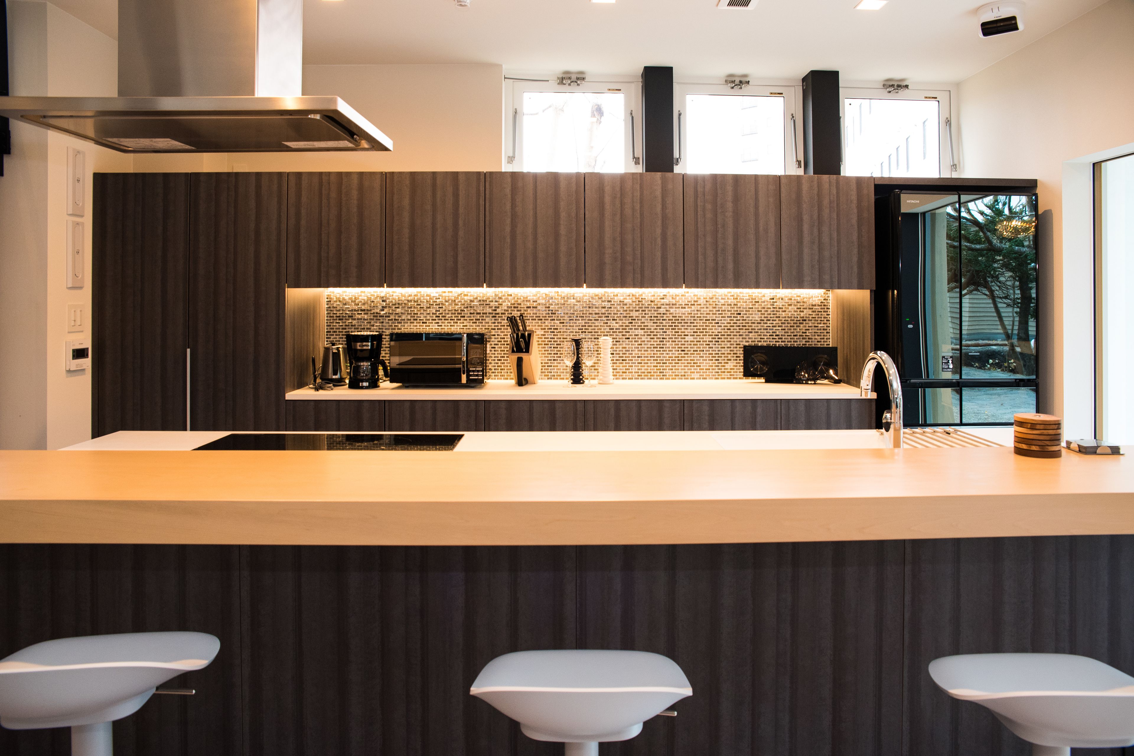 Una cocina moderna con una isla central, muebles oscuros y vistas al exterior a través de amplios ventanales.