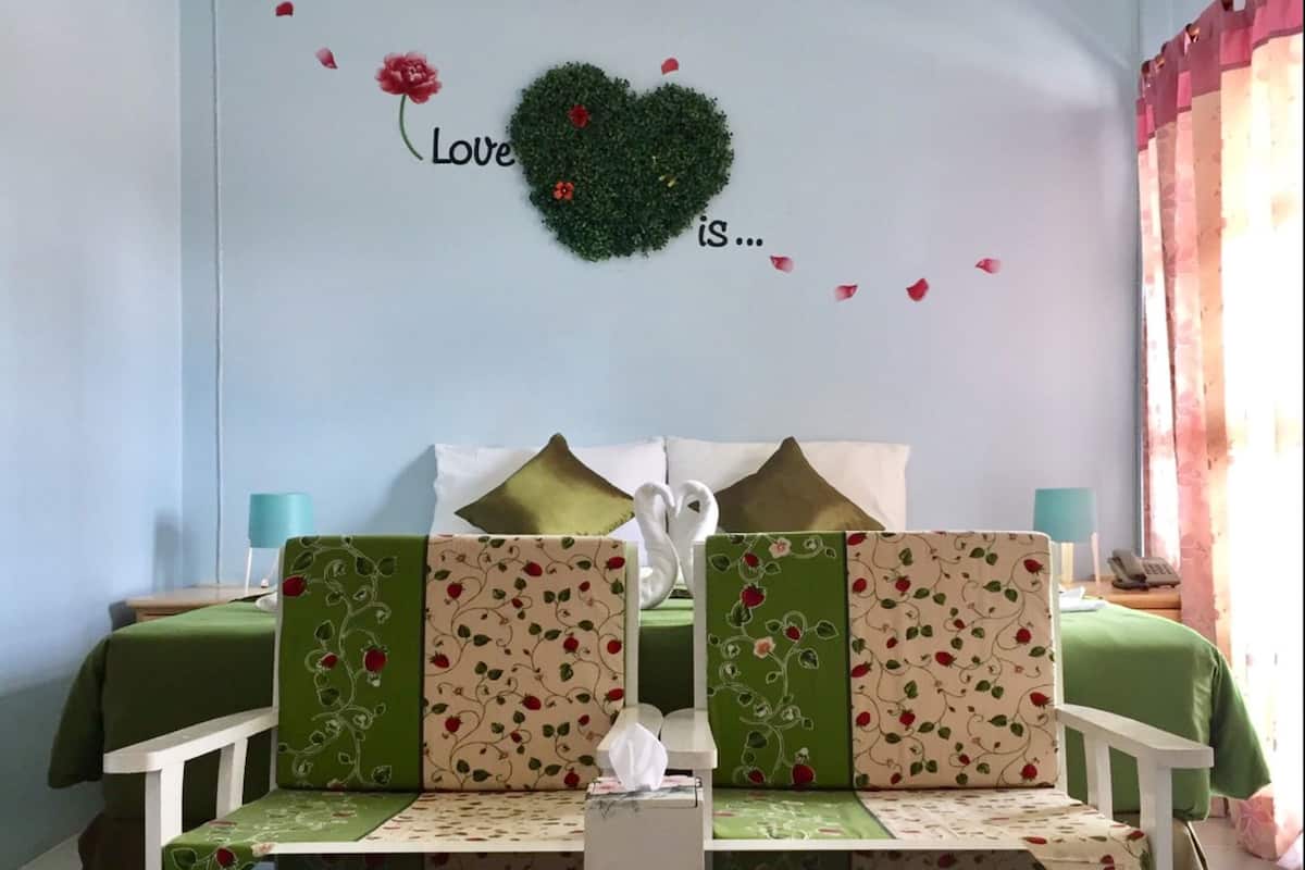 Een slaapkamer met een bed, twee stoelen, een klein tafeltje en een decoratieve wand met een hart en tekst.