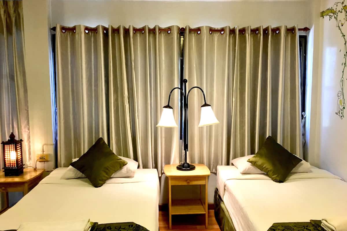 Een hotelkamer met twee bedden, een nachtkastje met een lamp en een gordijnen achtergrond.