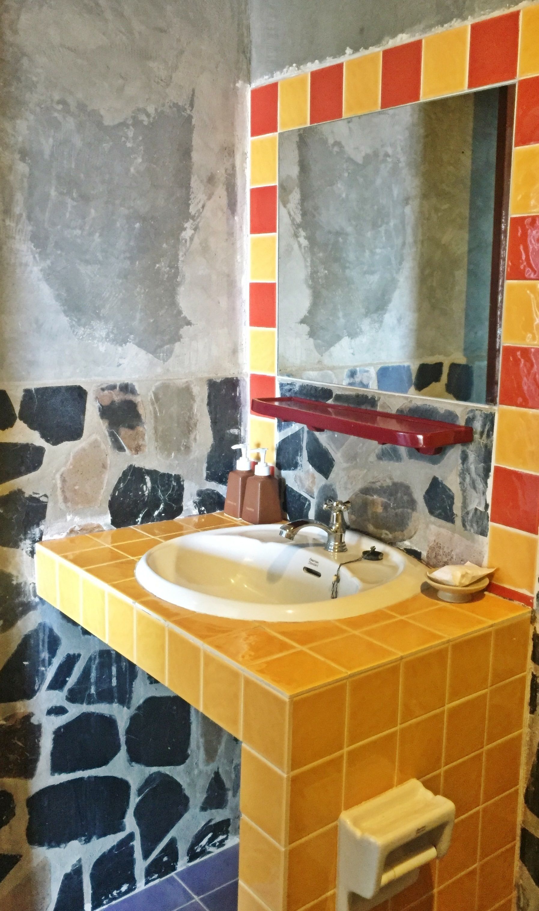 A bathroom with a stone wall, a yellow sink, and a mirror with a colorful border.