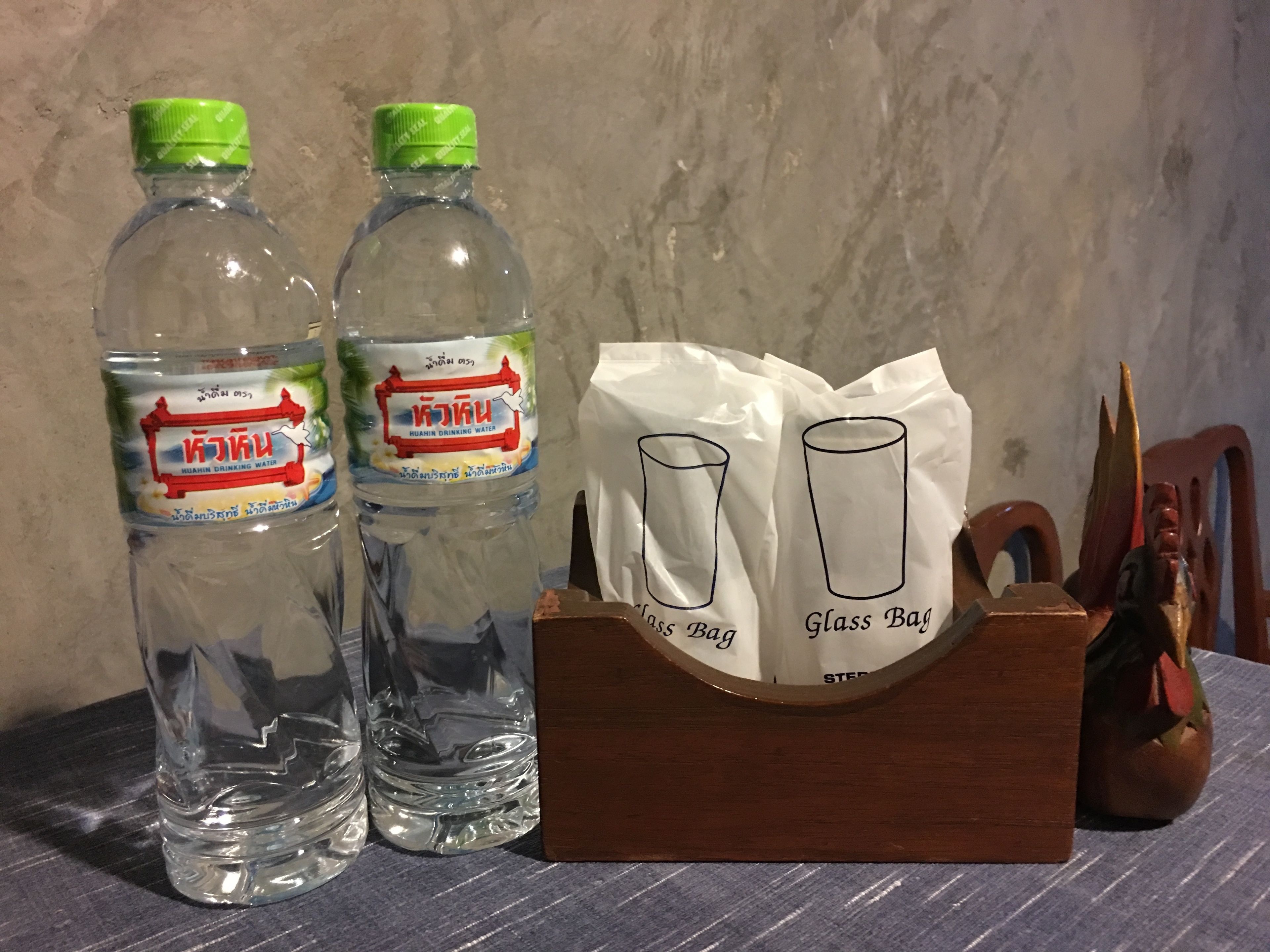 Deux bouteilles d’eau minérale Huamin et un ensemble de verres dans un sac, le tout posé sur un présentoir en bois.