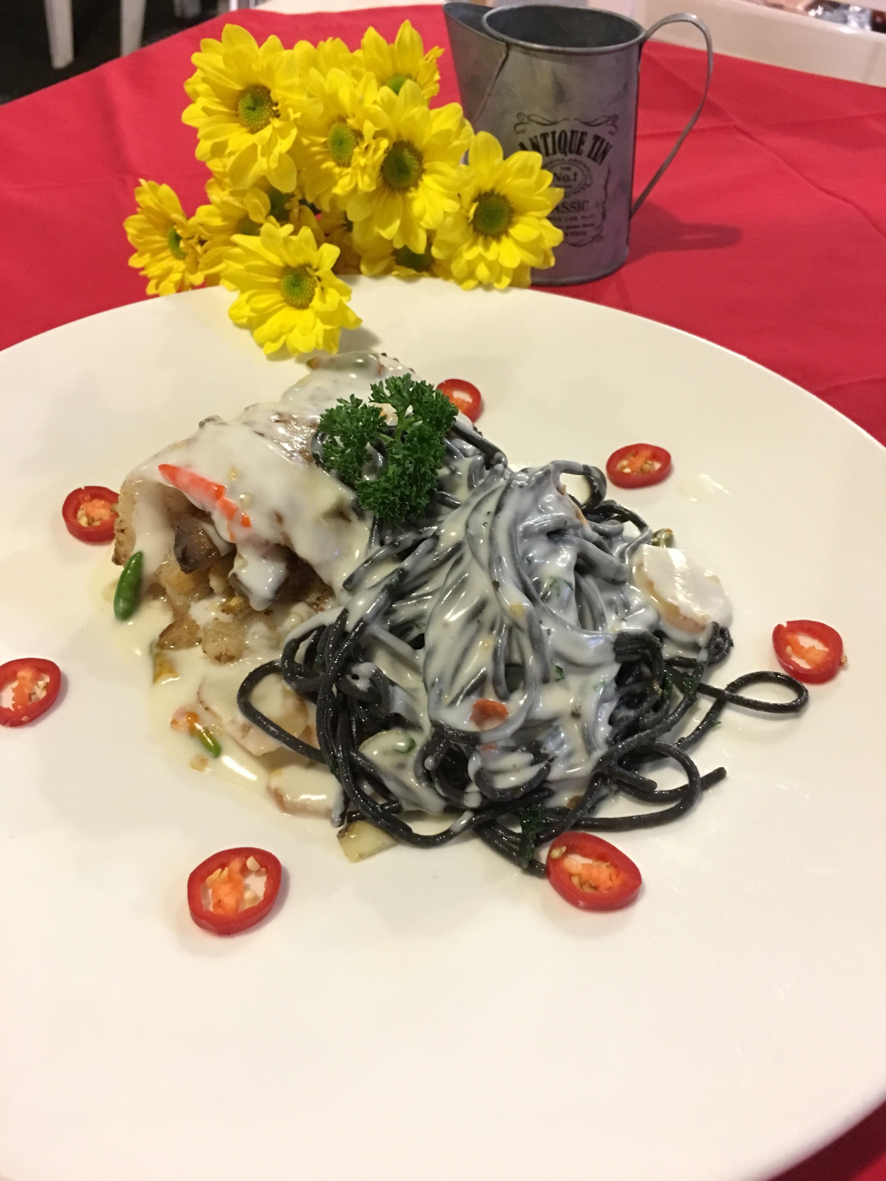 A plate of pasta with a creamy sauce, garnished with parsley and chili slices, on a white plate.