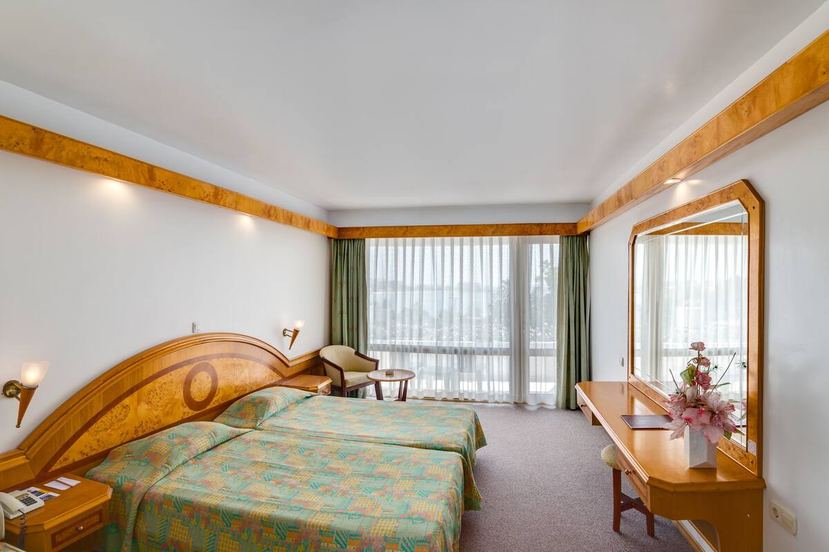 A hotel room with two beds, a desk, a chair, a nightstand, and a large mirror.