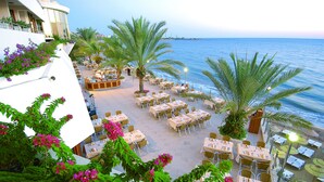 An outdoor dining area with tables and chairs, palm trees, and a view of the sea. - Rubi Hotel - All inclusive (Alanya)