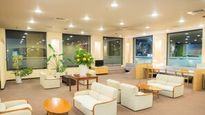 A spacious lobby with multiple seating areas, including sofas and chairs, a coffee table, and a small table with a vase of flowers.