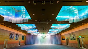 A spacious hall with a stage, ceiling lights, and artwork on the walls.