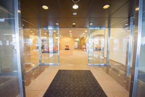 A hotel entrance with glass doors, a carpeted entrance, and a visible reception area in the background.