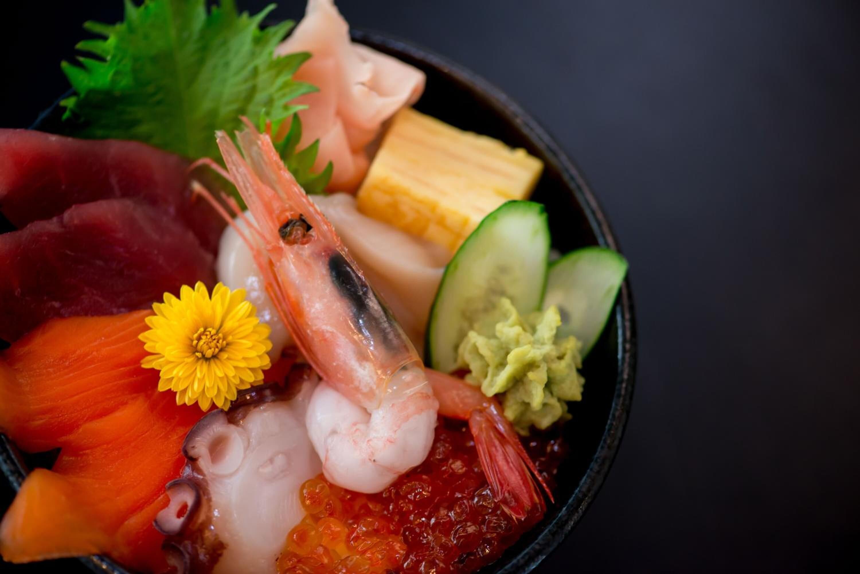 A bowl of sushi with various ingredients including shrimp, salmon, and avocado.