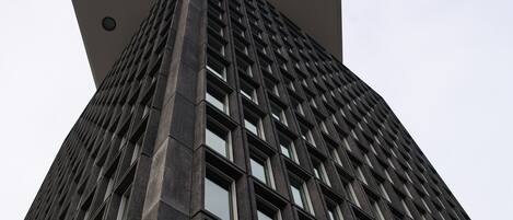 Un edificio alto con diseño arquitectónico moderno, que presenta una fachada con una cuadrícula de ventanas y una entrada destacada en la esquina.