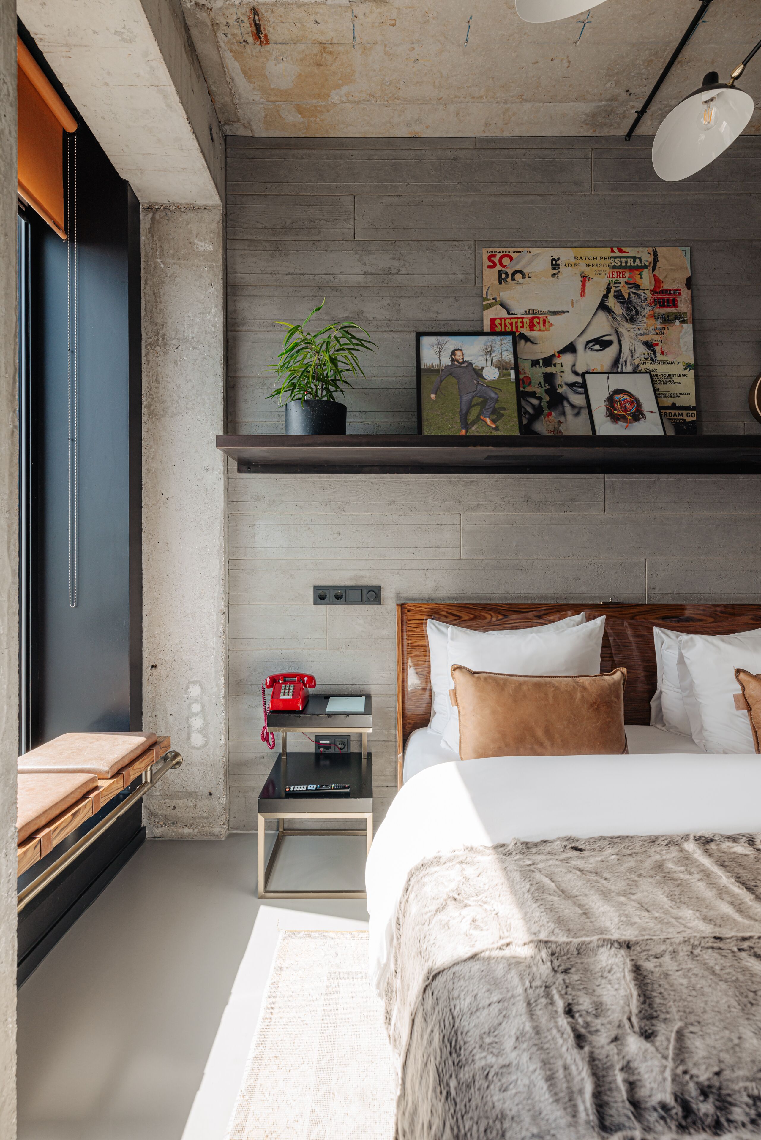 Un dormitorio moderno con un cabecero de madera, un teléfono rojo, una mesita pequeña y una cama grande con una manta mullida.