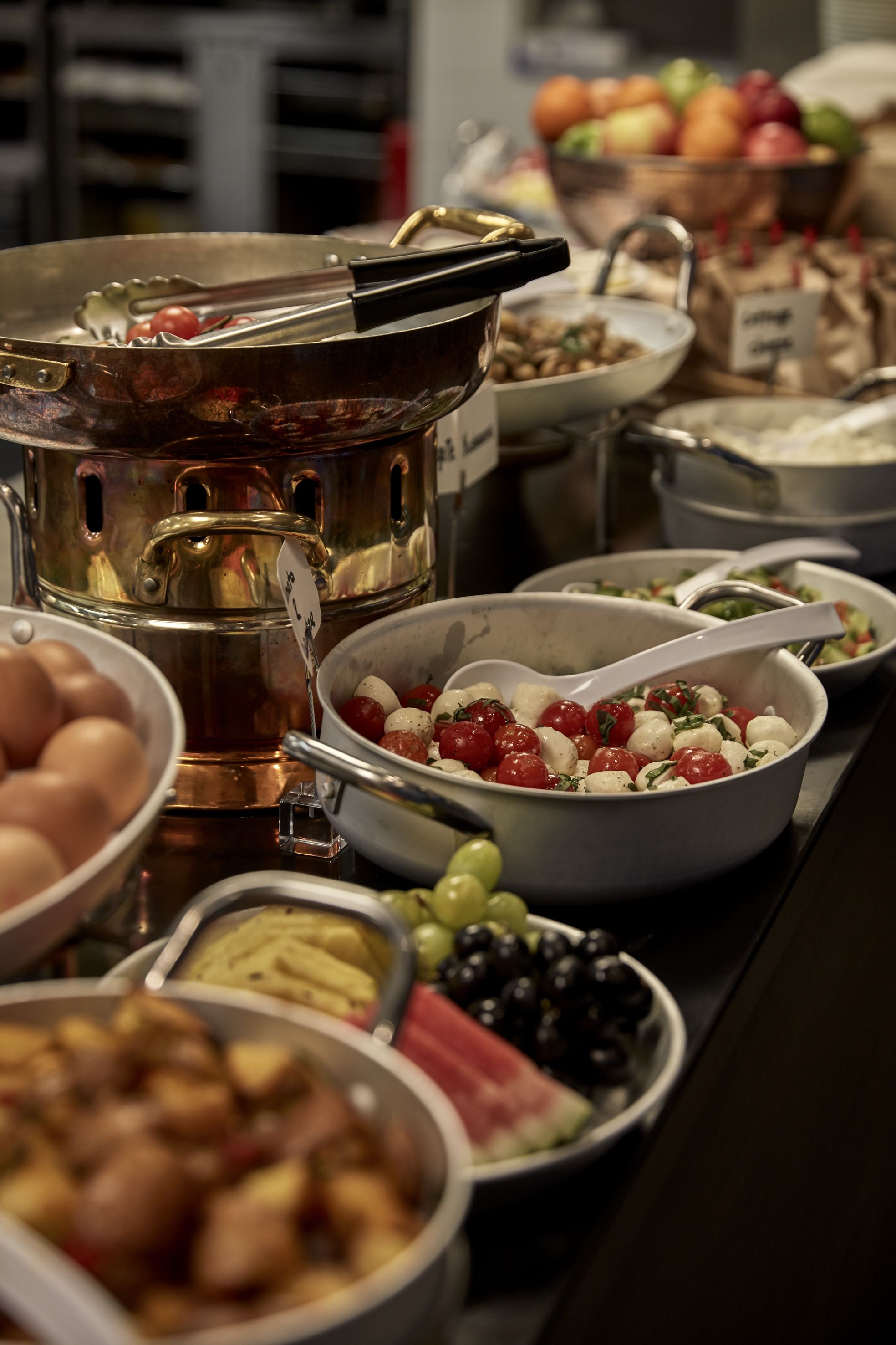 A buffet with various dishes including a large pot, bowls of food, and a bowl of fruit.
