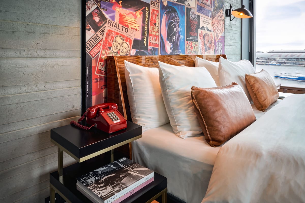 A hotel room with a bed, pillows, a nightstand with a book and a red telephone.